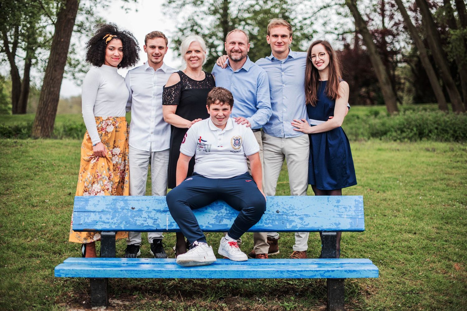 Family members seated together on bright blue bench in park setting.