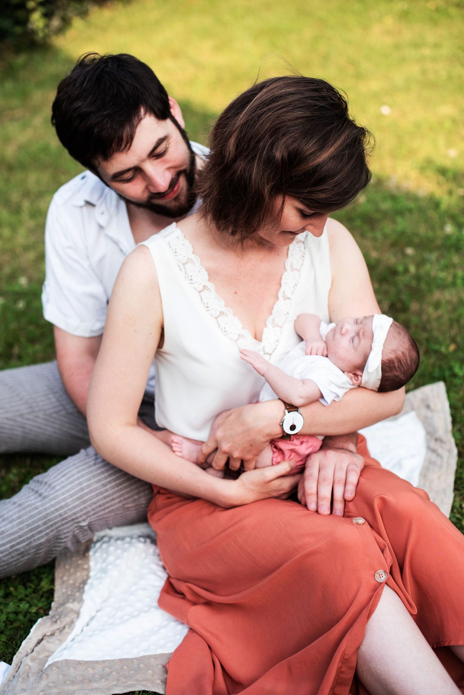 Family bonding moments captured outdoors on grass with white and coral colored clothing.
