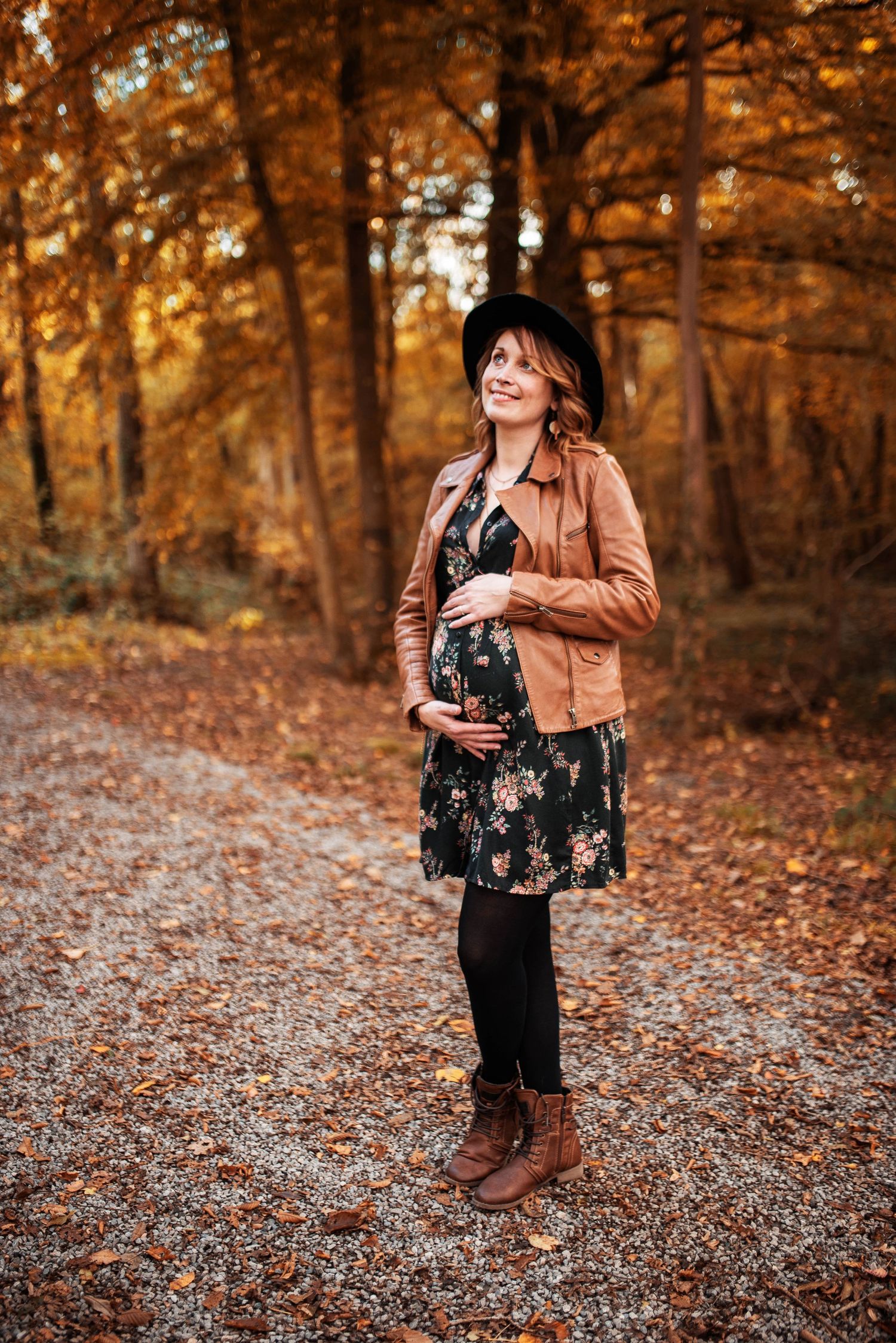 Maternity portrait session in fall forest with brown leather jacket and floral dress.