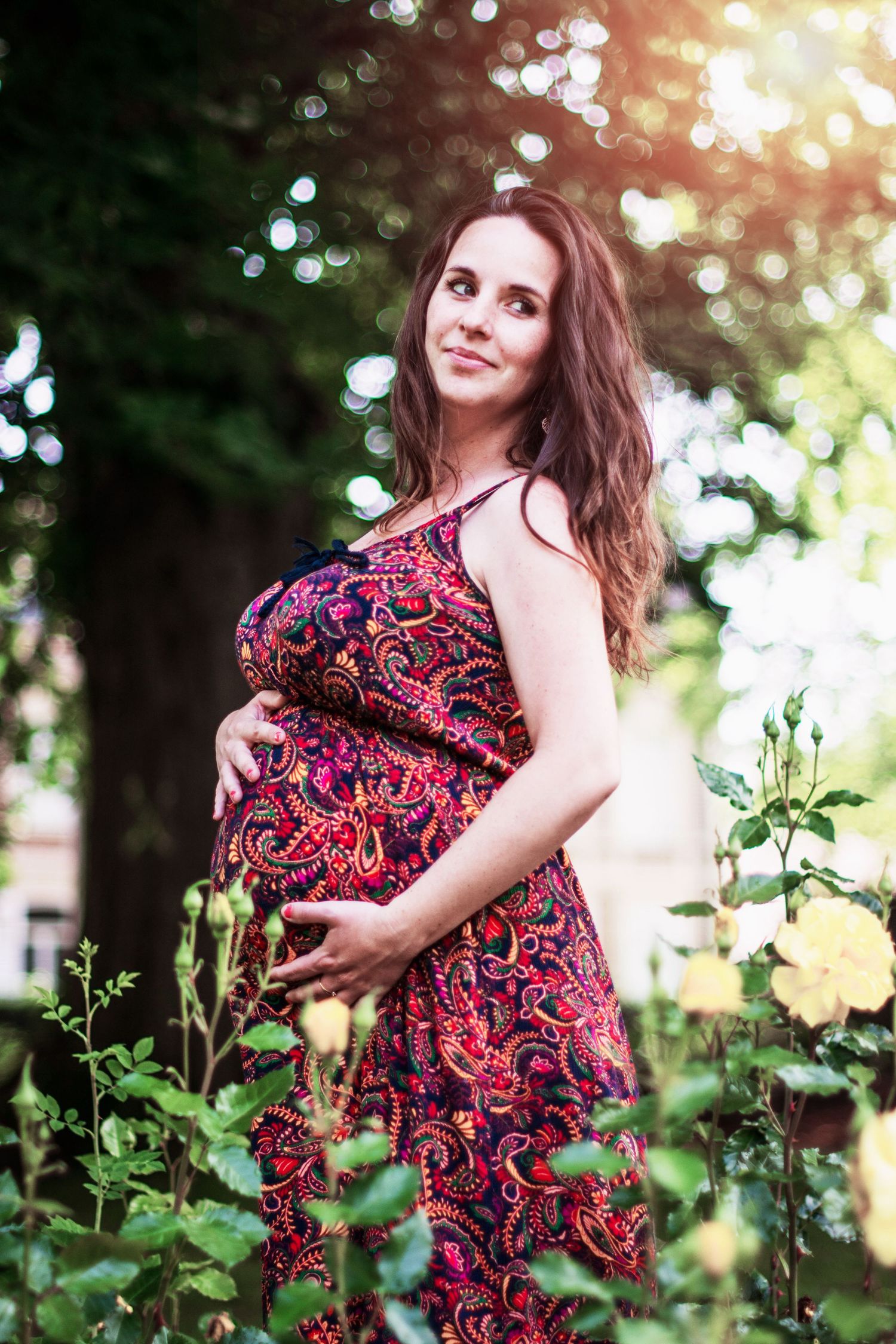 Floral maternity photoshoot in a garden with red and pink patterned dress.
