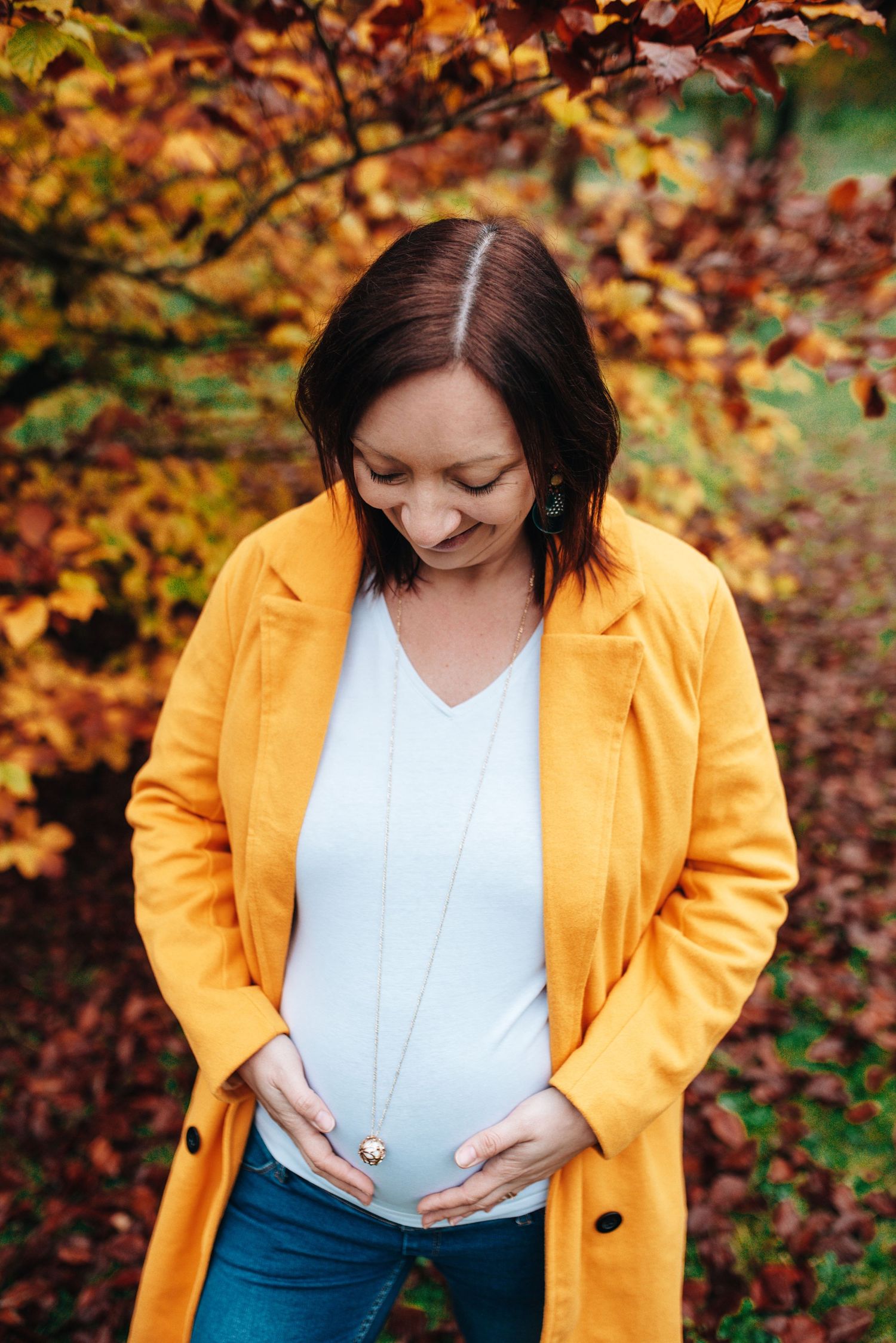 Fall maternity photos featuring a bright yellow coat and white top against autumn foliage.
