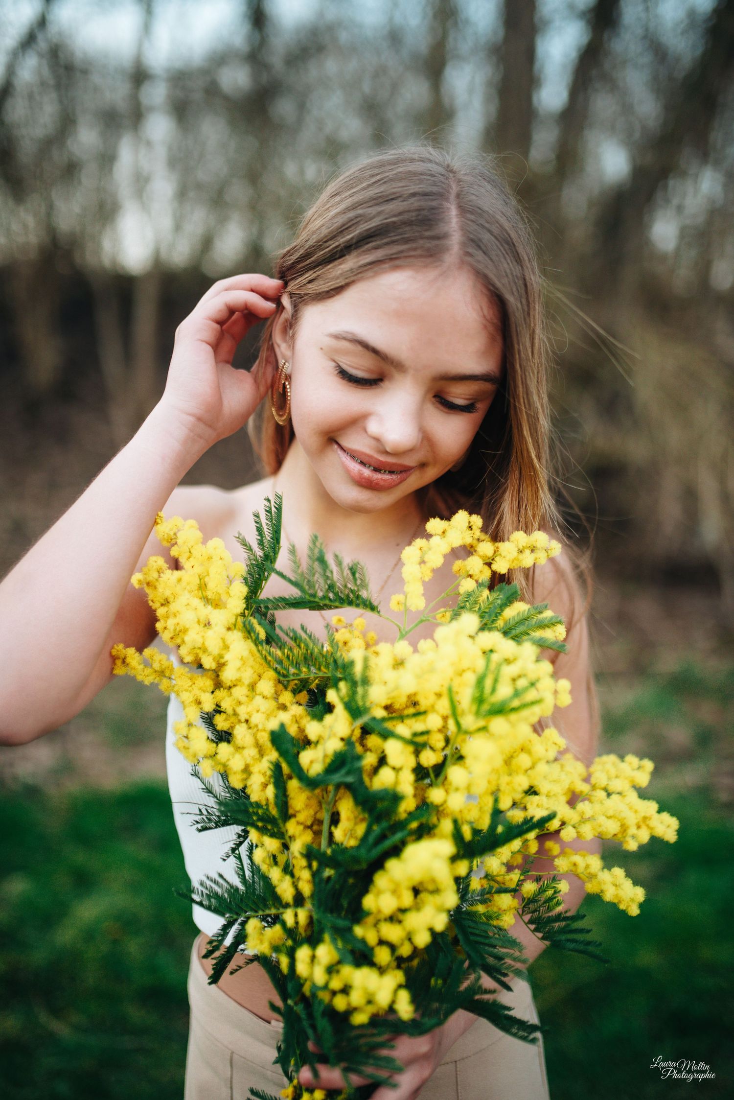 Woman holding bright yellow mimosa flowers against a natural woodland background.