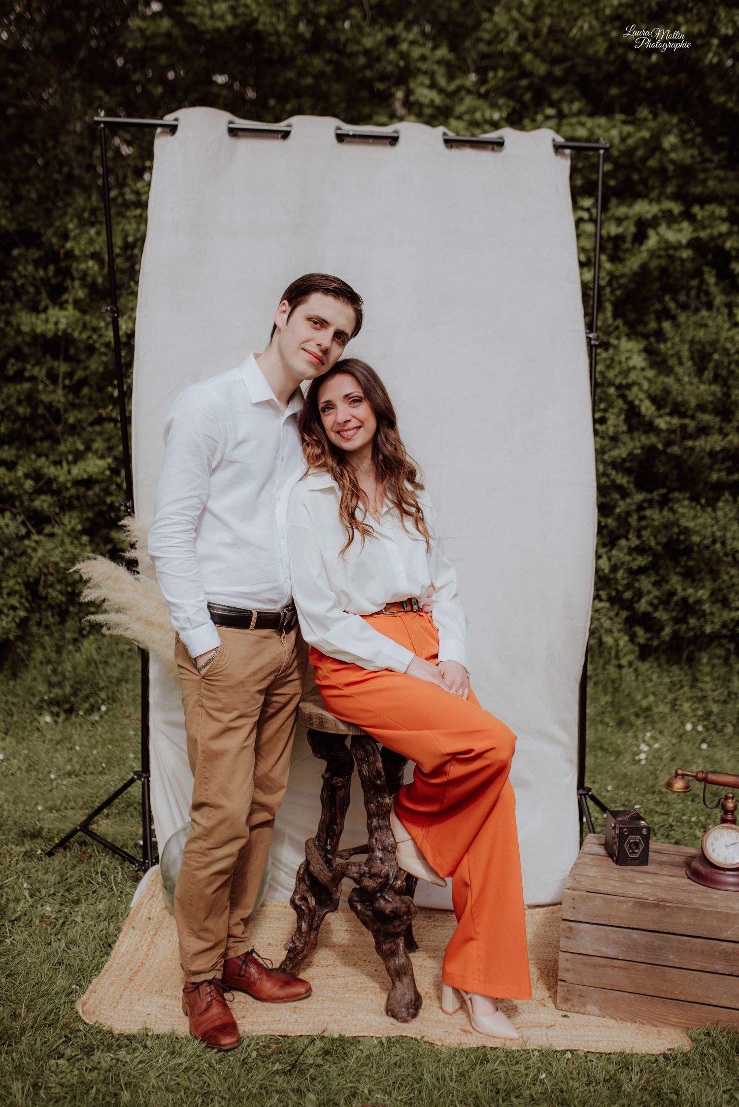 Couple in casual attire poses against white backdrop in outdoor photoshoot series.