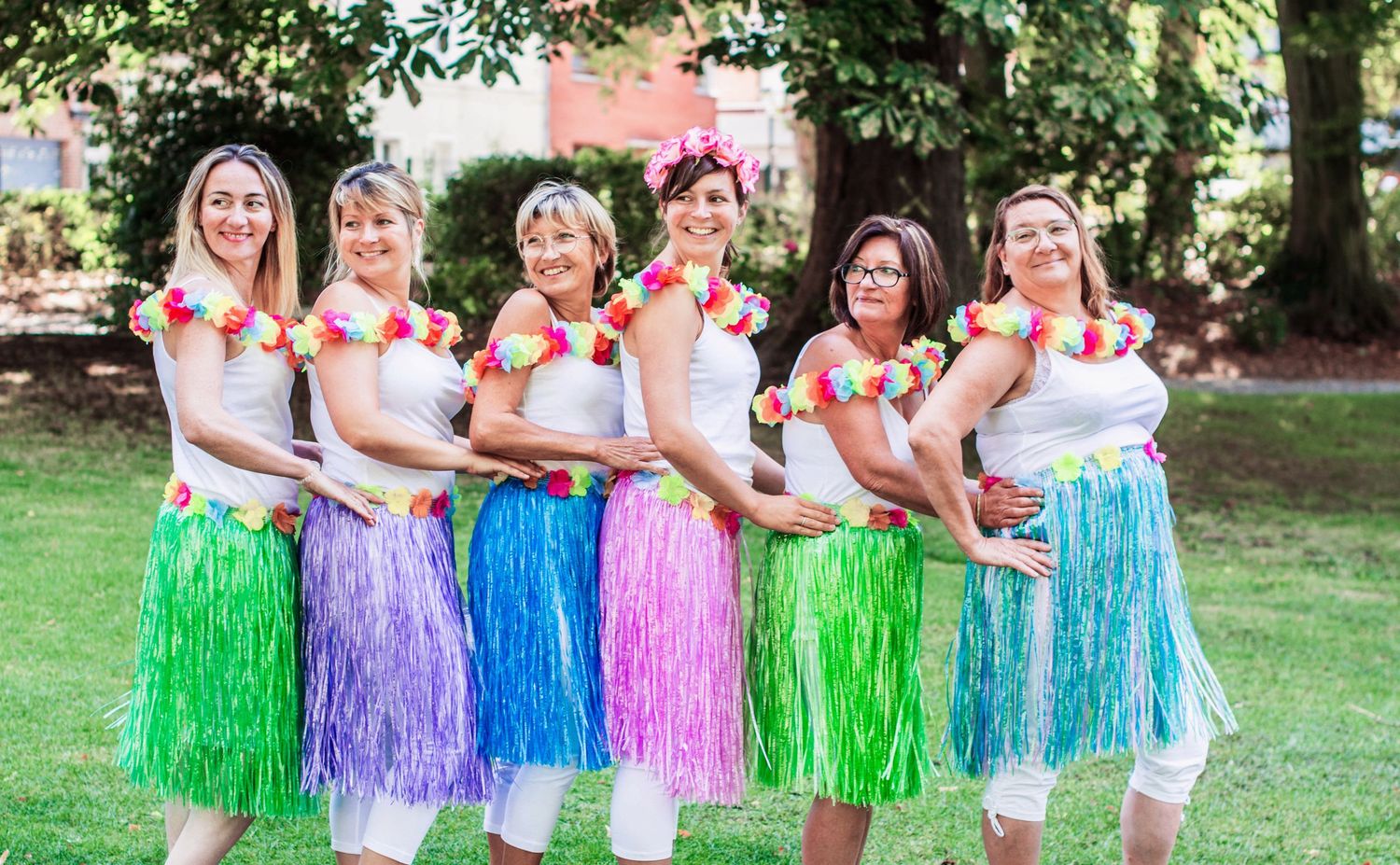 Group wearing colorful grass skirts poses outdoors in a fun summer photoshoot.