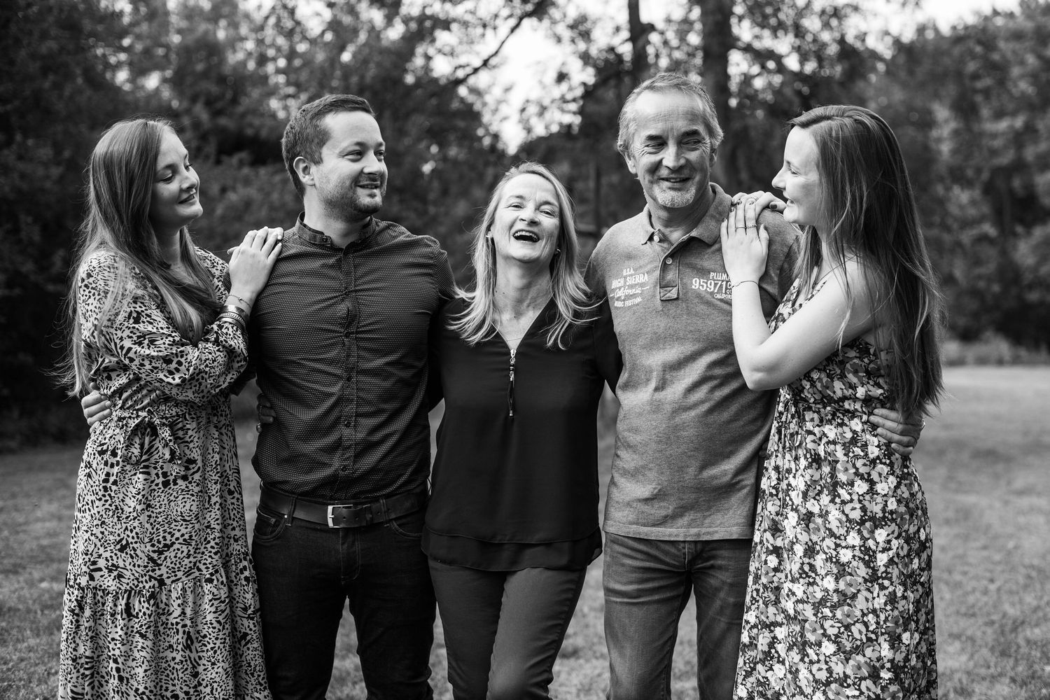 A candid black and white family photo of five people laughing together outdoors.