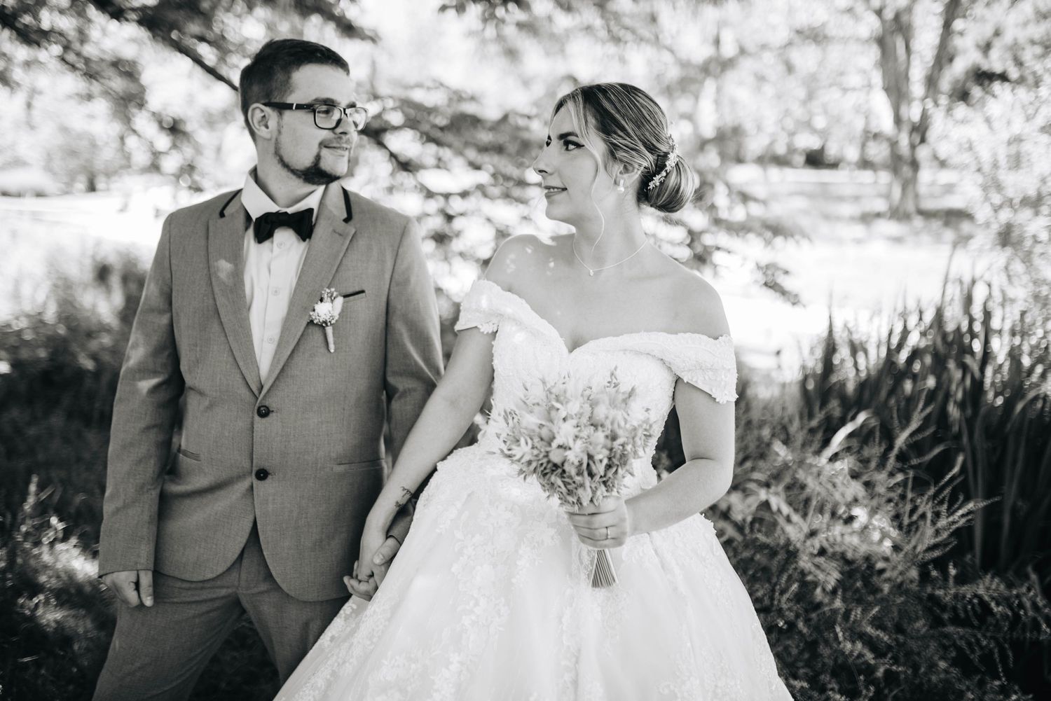 A romantic outdoor wedding portrait featuring a couple in formal attire surrounded by natural greenery.