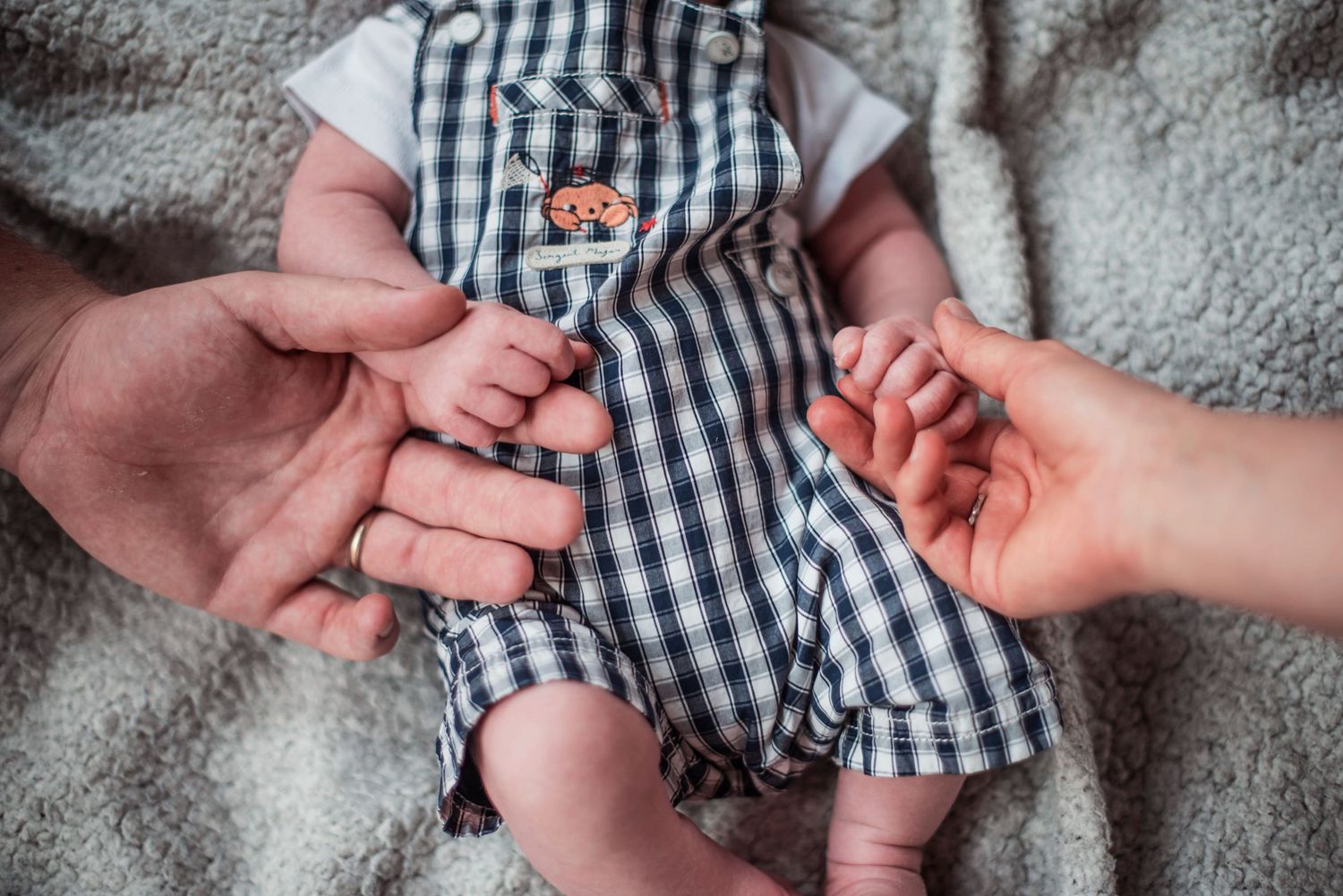 Close-up series of tiny baby feet and hands in black and white checkered clothing against a textured background.