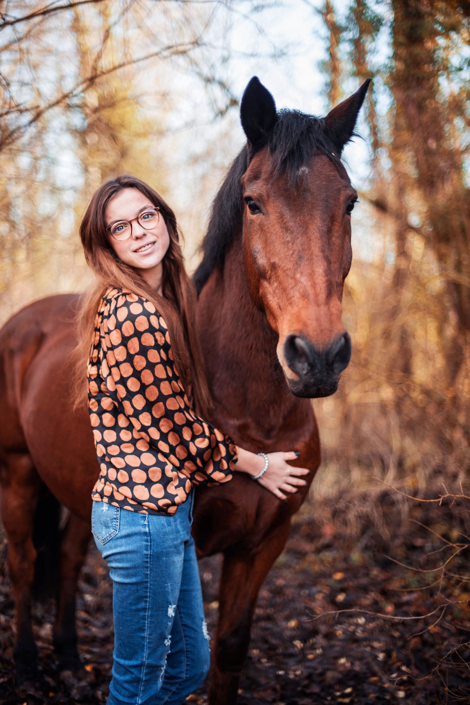Brown horse and person in patterned sweater in autumn forest setting.