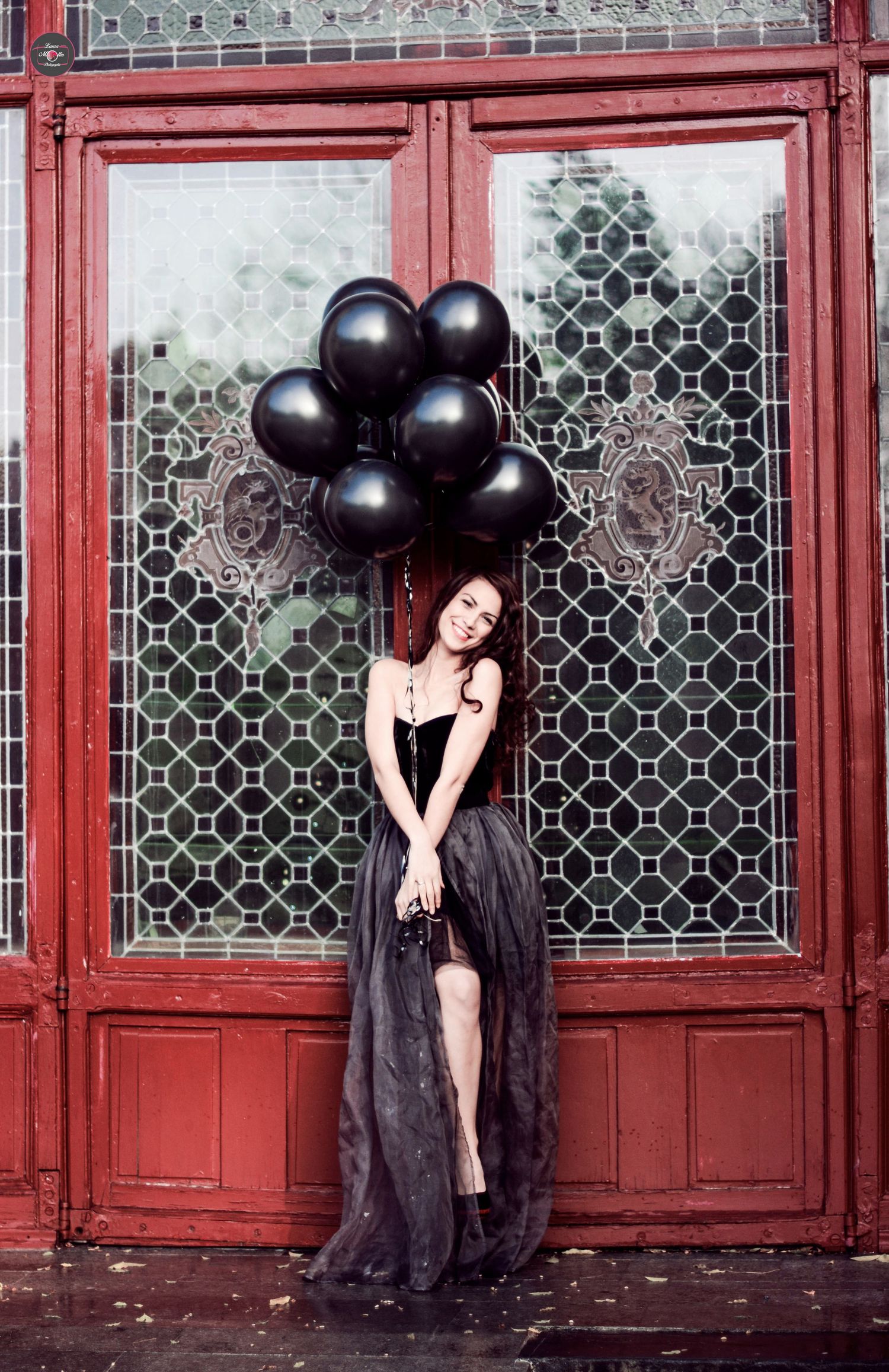 Moody fashion photoshoot featuring black balloons and red doorway architectural details.