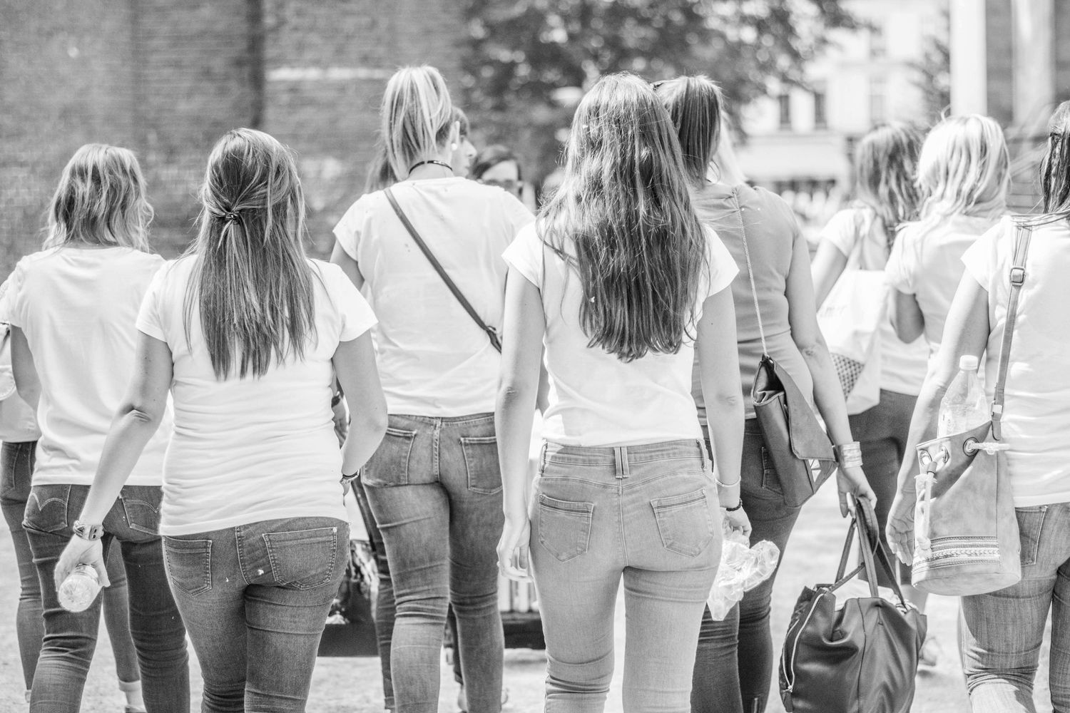 Row of women wearing matching white tops and jeans standing together outdoors.