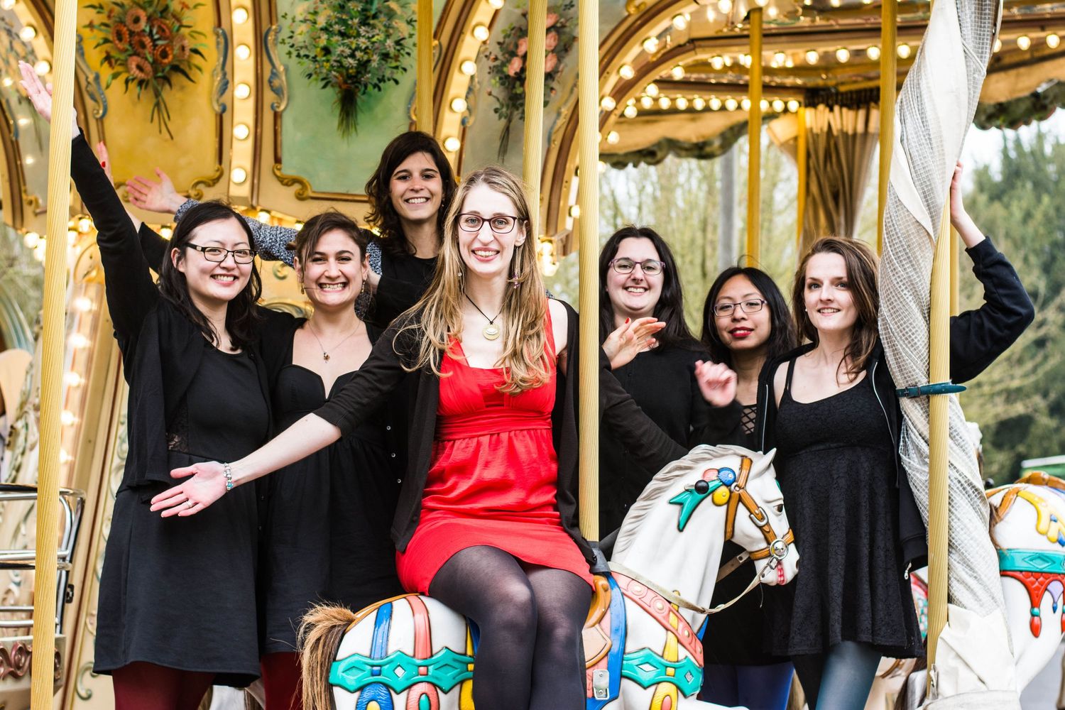 Group of friends posing playfully together on a carousel in matching outfits at an outdoor location.