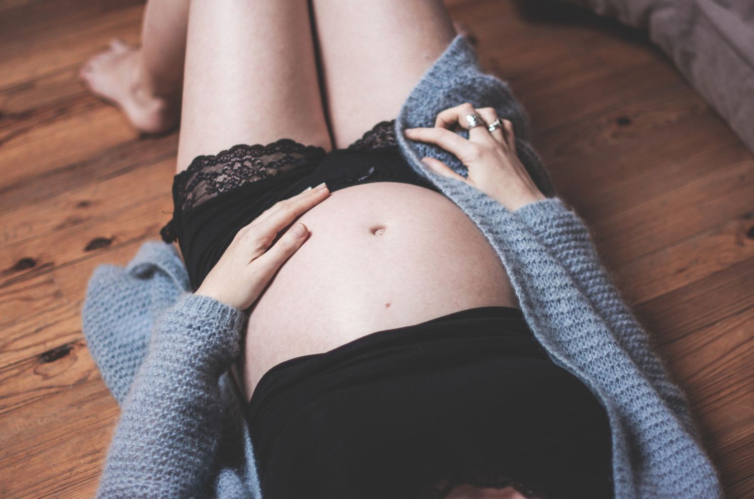 Intimate maternity boudoir photo series on wooden floor with cozy gray sweater.