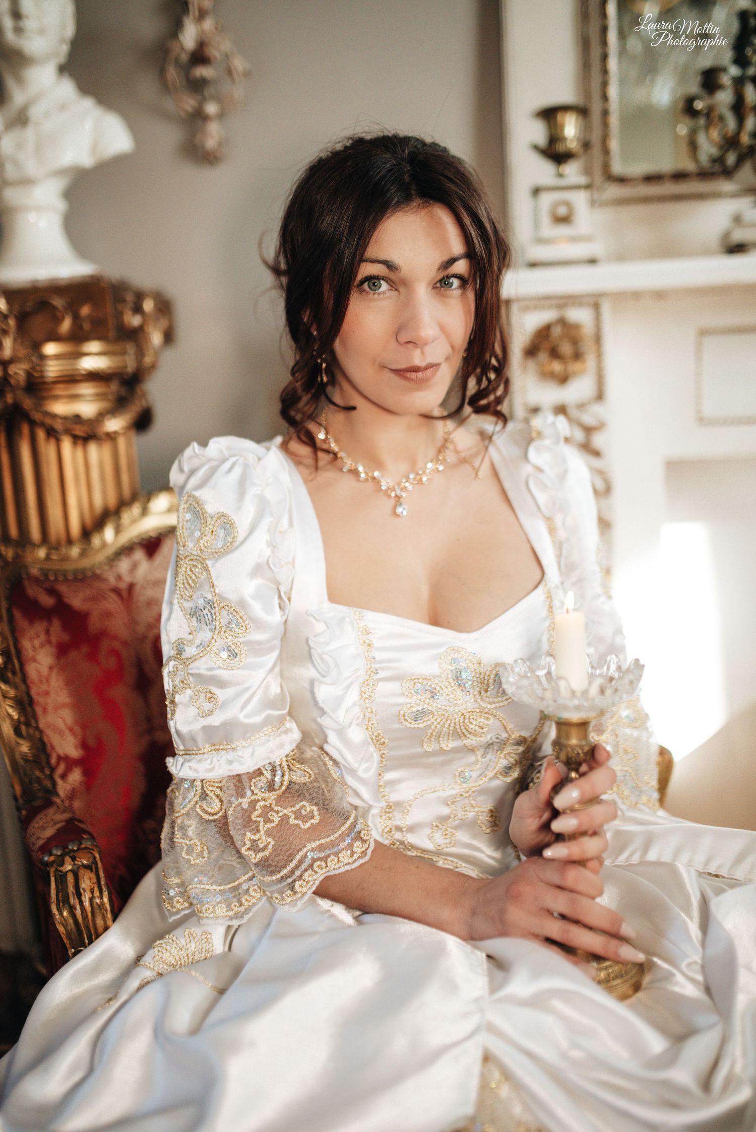 Woman in elegant white satin and lace Regency-style dress poses in vintage interior setting.