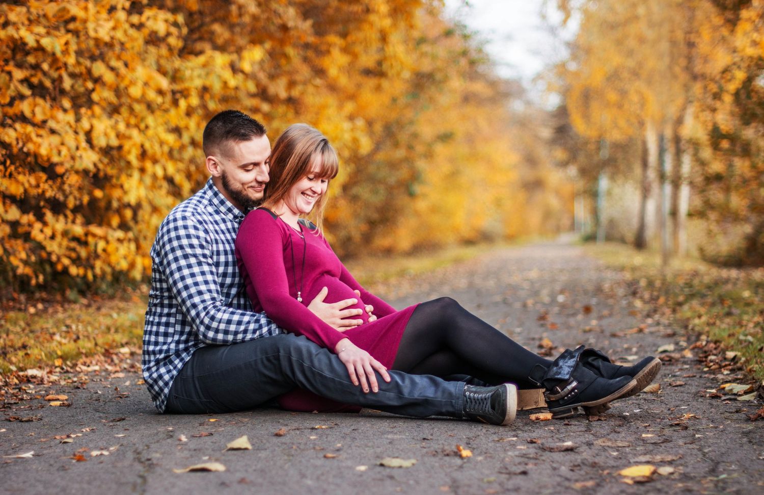 Couple walking together on a path lined with golden autumn trees and fallen leaves.