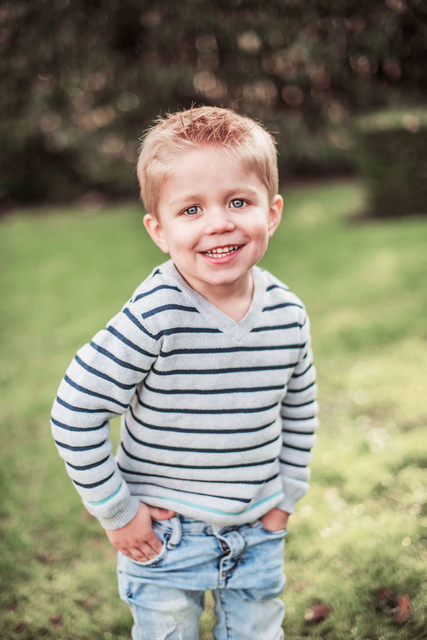 Young child in striped shirt and jeans playing outdoors on a sunny day.