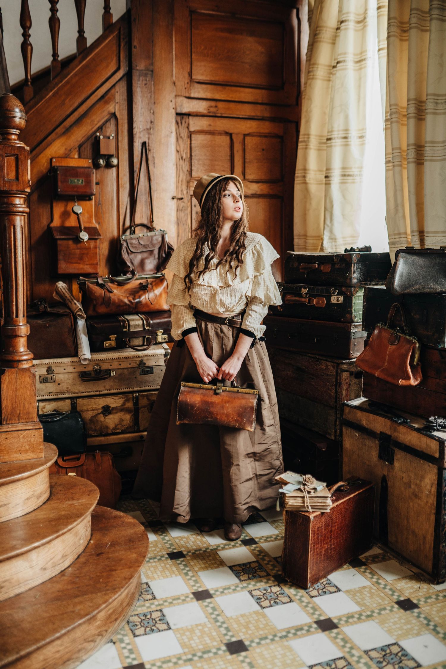 Woman in vintage attire holding a leather bag surrounded by antique trunks in a rustic wooden interior.