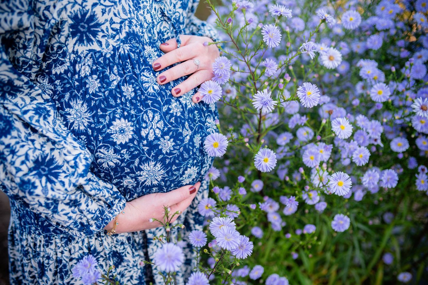 Close-up shots of hands cradling a pregnant belly among purple wildflowers.