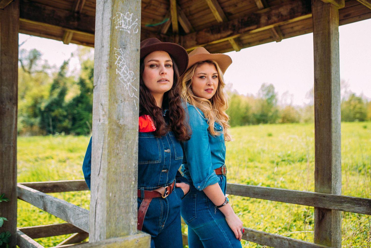 Friends in western-inspired denim outfits posing together on a covered wooden porch.