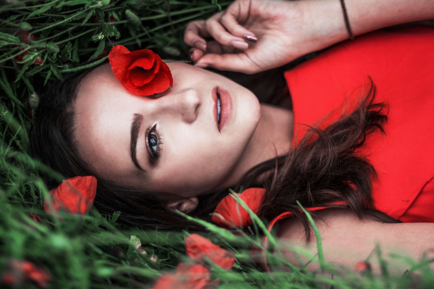Artistic portrait of someone lying in grass surrounded by red poppies.