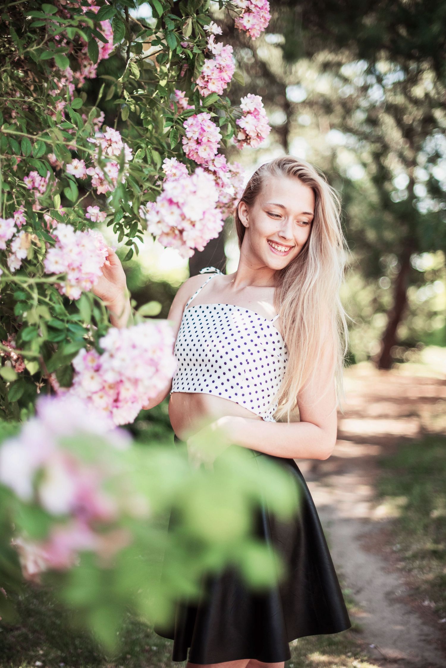 Spring portrait with blooming pink flowers and polka dot top in garden setting.