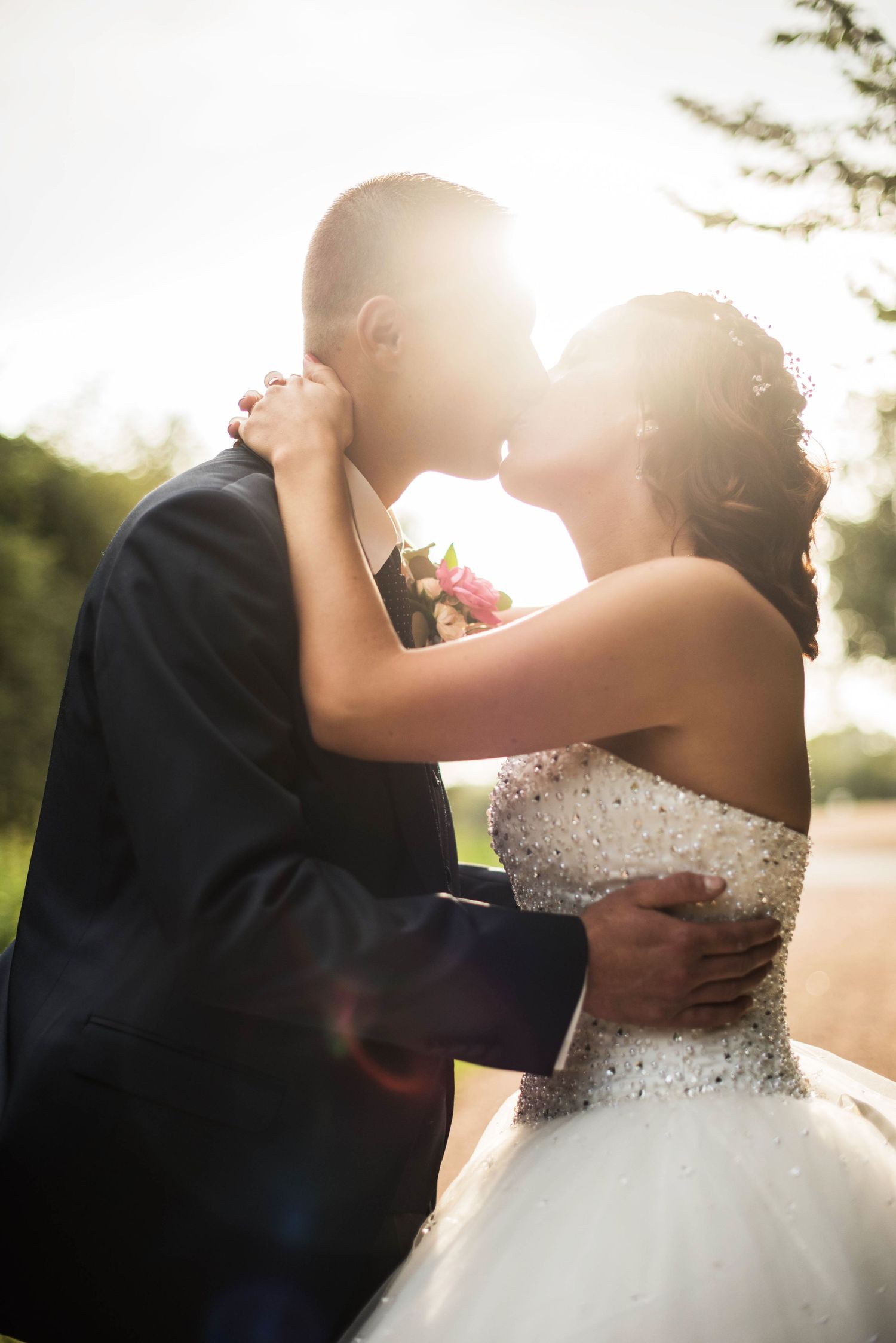 A backlit wedding portrait captures a romantic embrace with sunlight creating a dreamy effect.