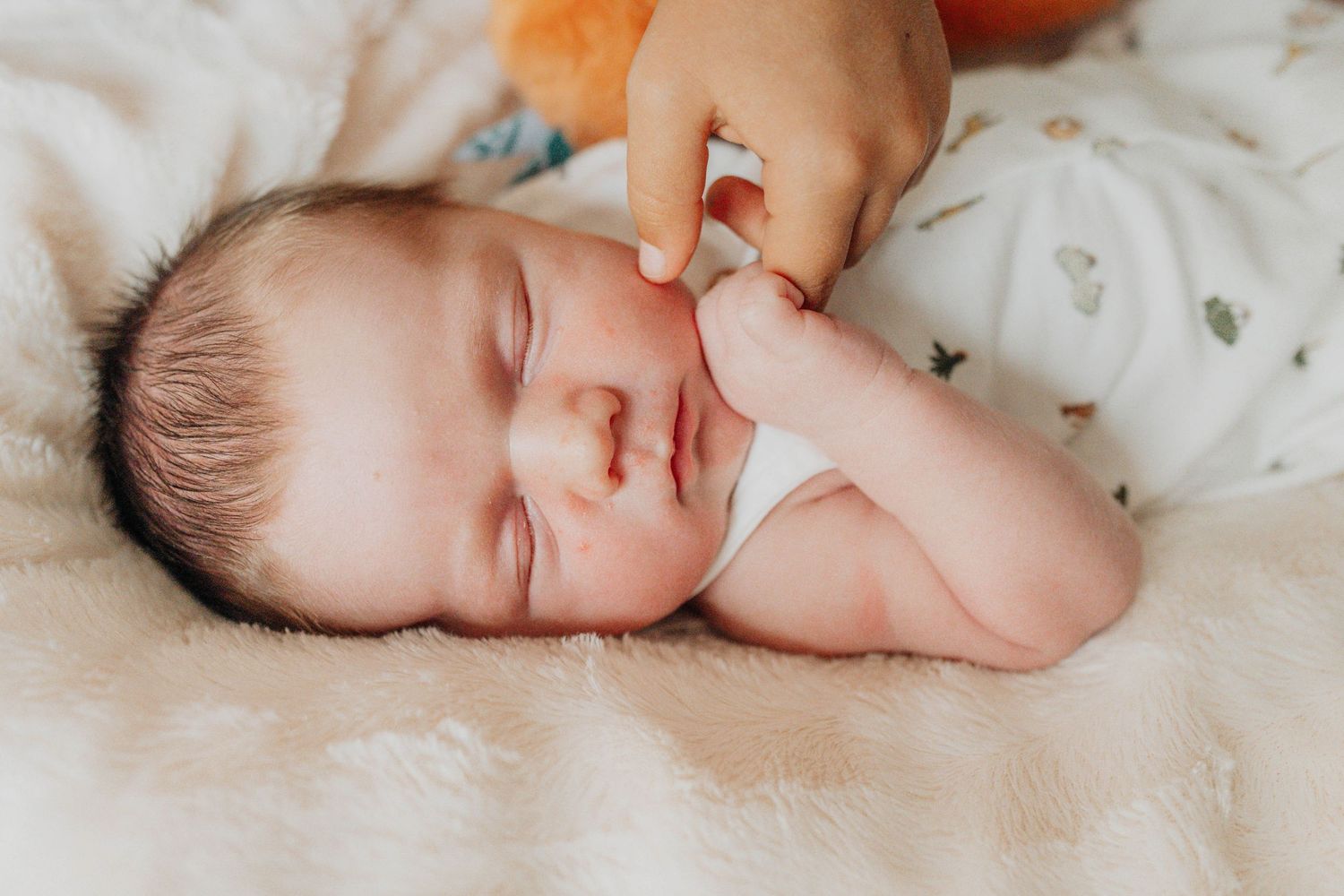 A sleeping baby photographed in warm natural light on soft bedding.