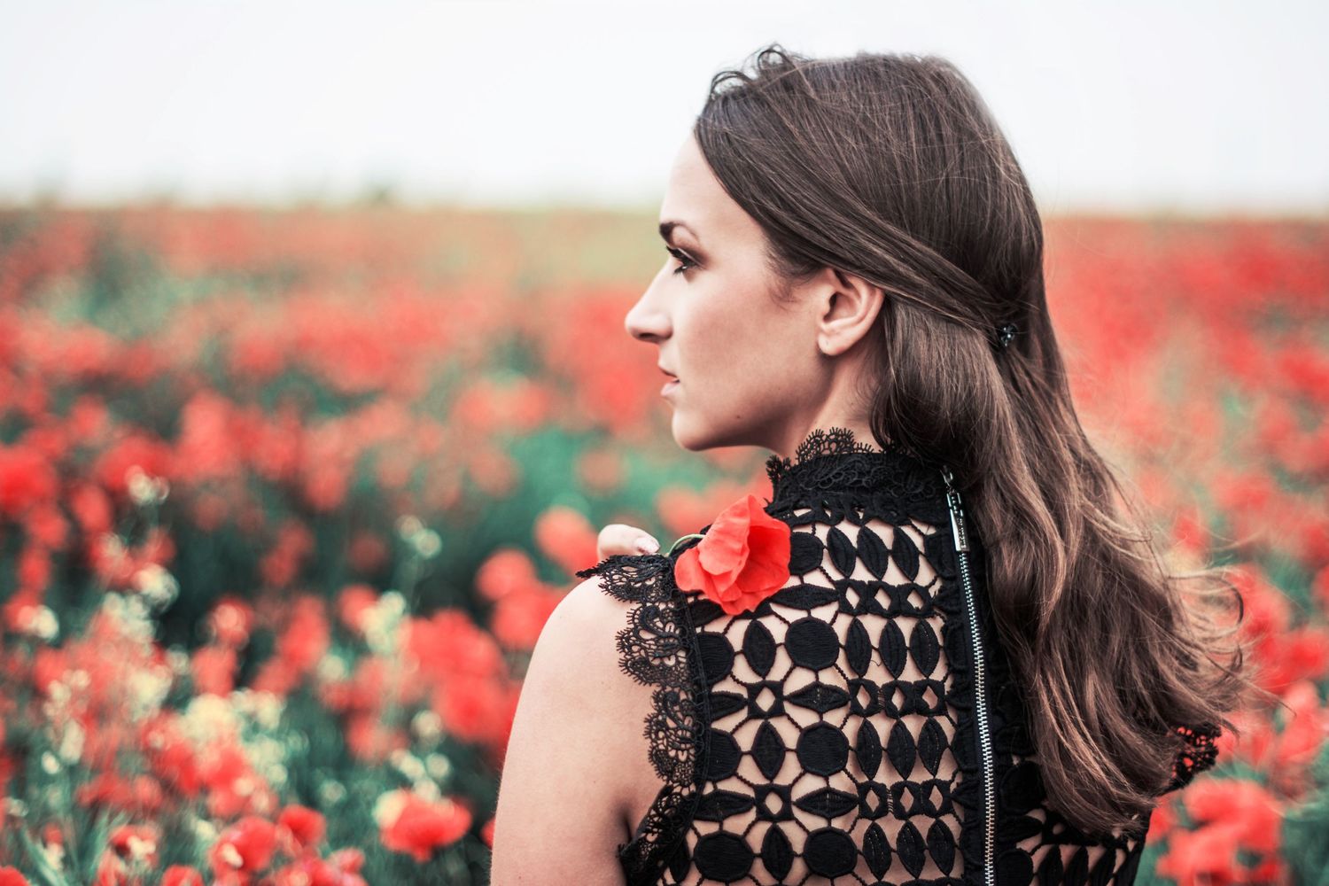Profile view in a poppy field wearing an ornate black crochet top with red flower accent.