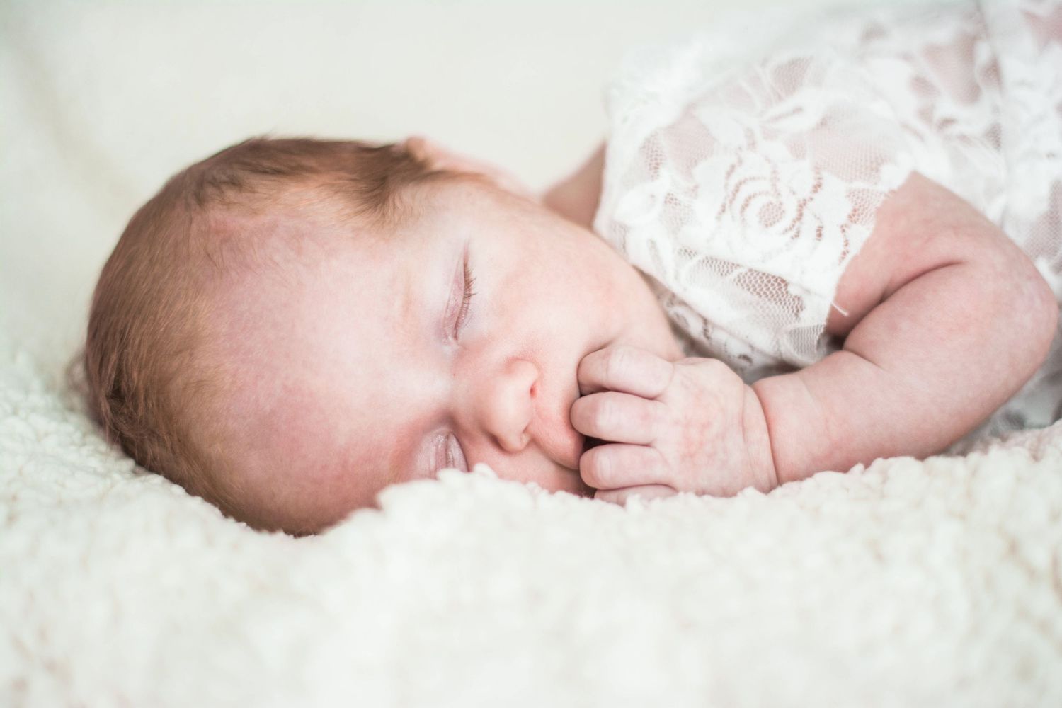 Newborn baby sleeping peacefully on white textured blanket.