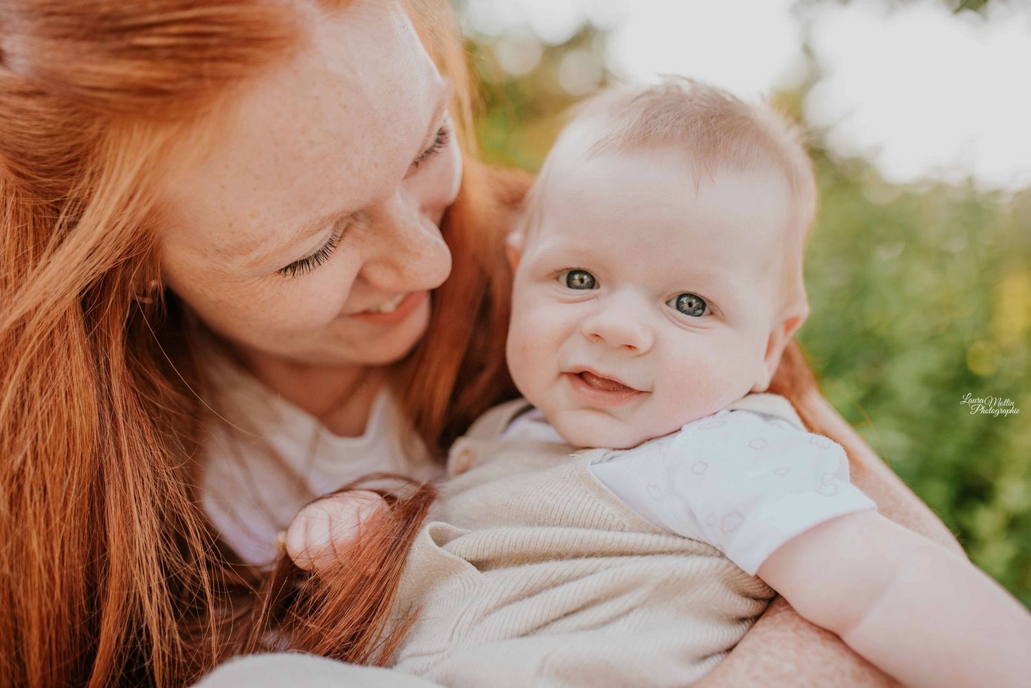 Tender outdoor family moment captured in warm sunlight with natural greenery background.