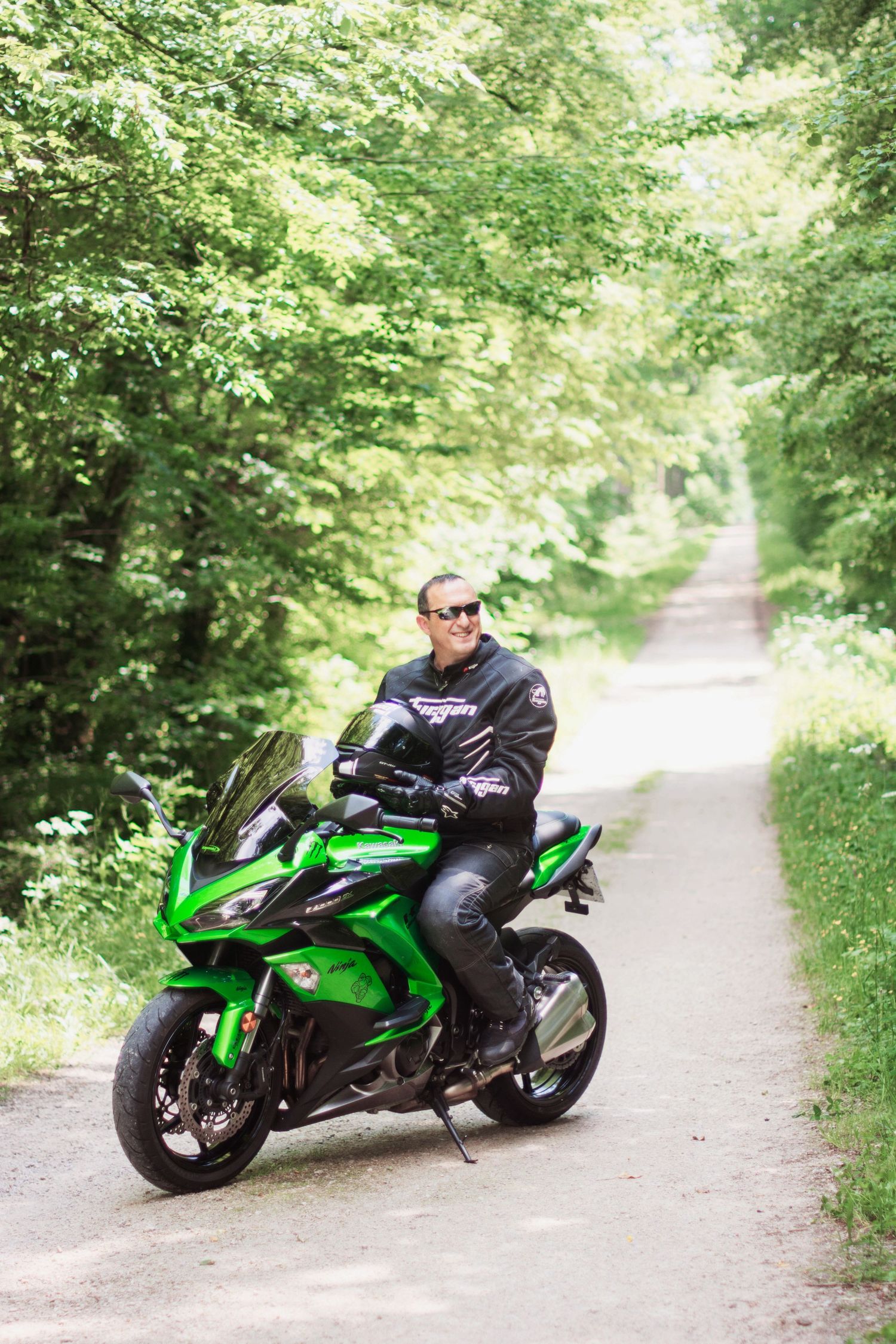 Sport bike rider on green Kawasaki motorcycle cruising through wooded path.