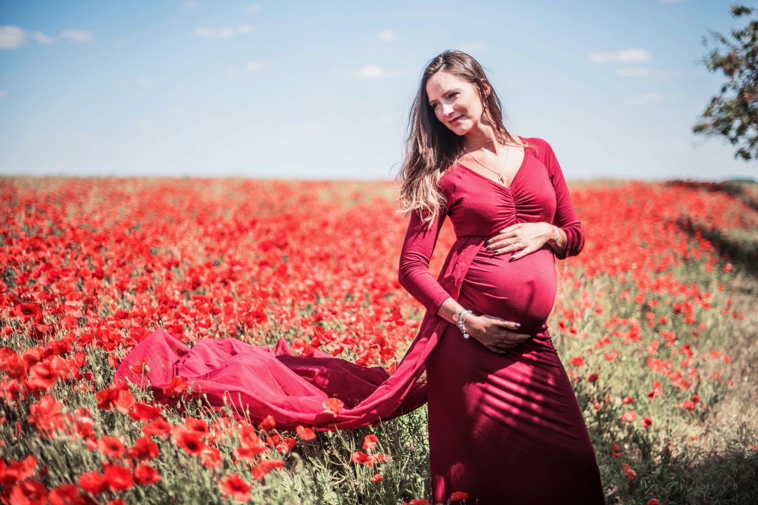 Flowing red dress maternity photos in blooming poppy field on sunny day.