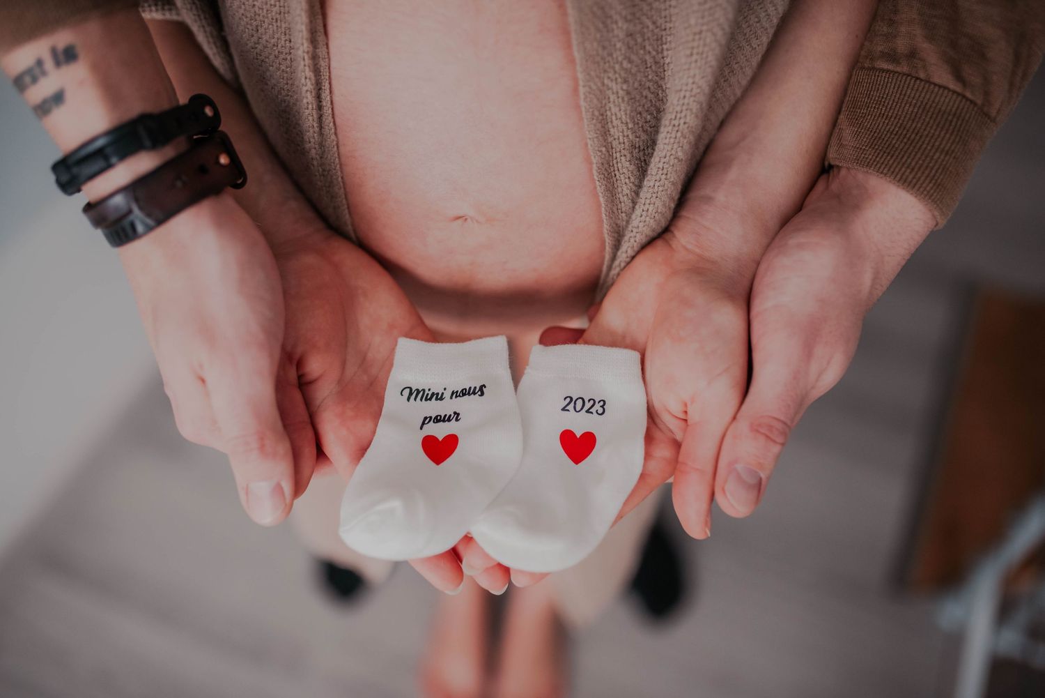 Close-up of hands holding tiny baby shoes against a neutral background.