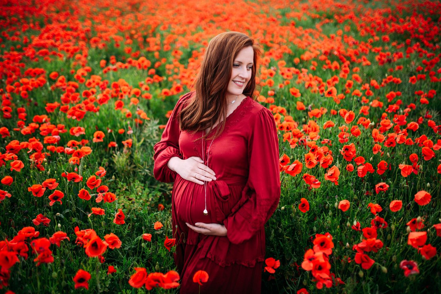 A flowing red dress stands out in a stunning field of blooming orange poppies.