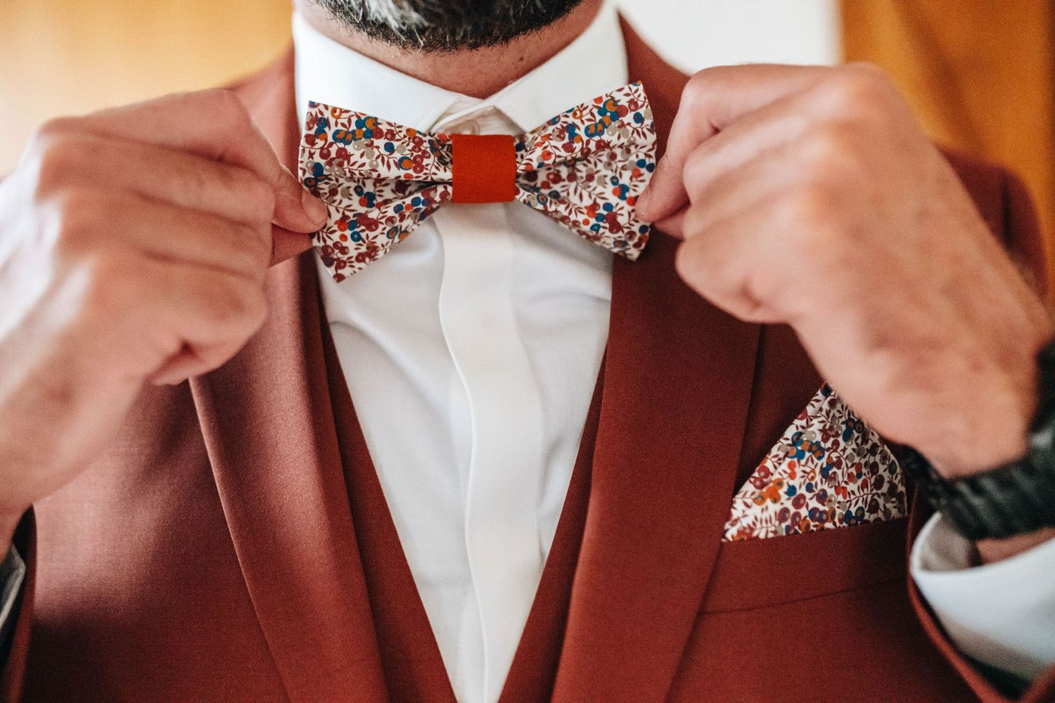 Close-up details of a floral bowtie being adjusted on a white dress shirt.