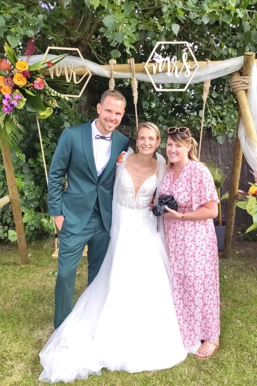 Wedding photographer capturing couple under rustic wooden arch with floral decorations.