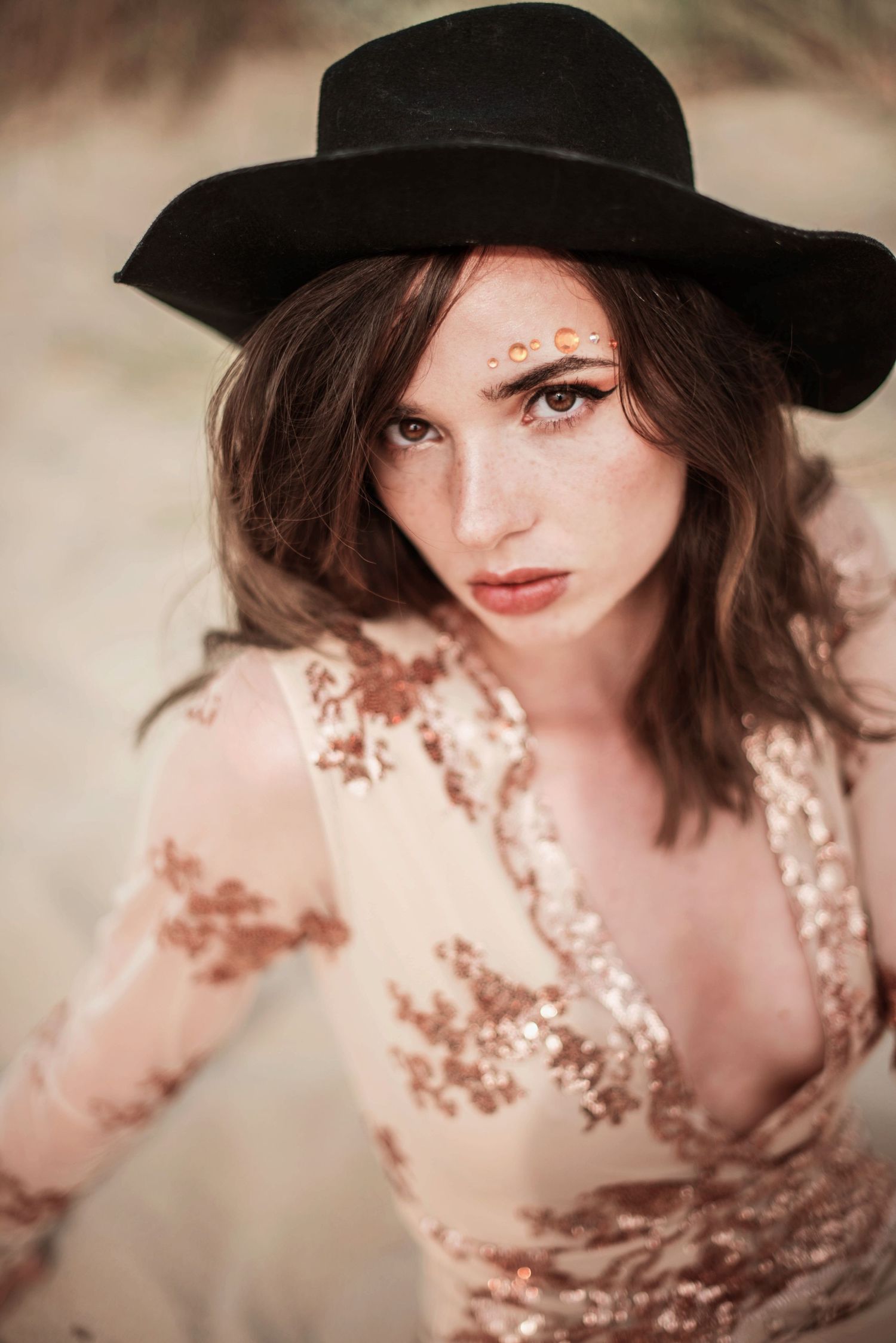 Artistic portrait of a person wearing a black hat and floral dress in soft sepia tones.