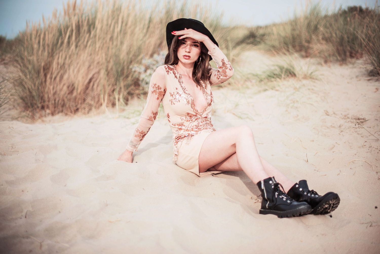 Fashion portrait of a person in pink dress and combat boots sitting on sandy beach.