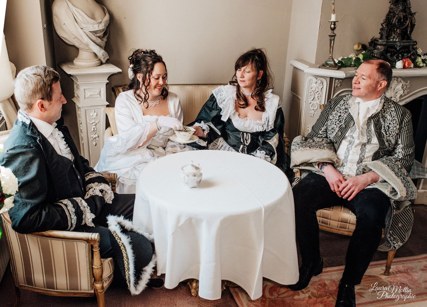 Tea party scene with guests in historical attire seated at round tables.