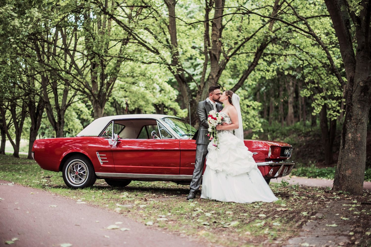 Wedding portraits in a lush green forest setting with vintage red car.