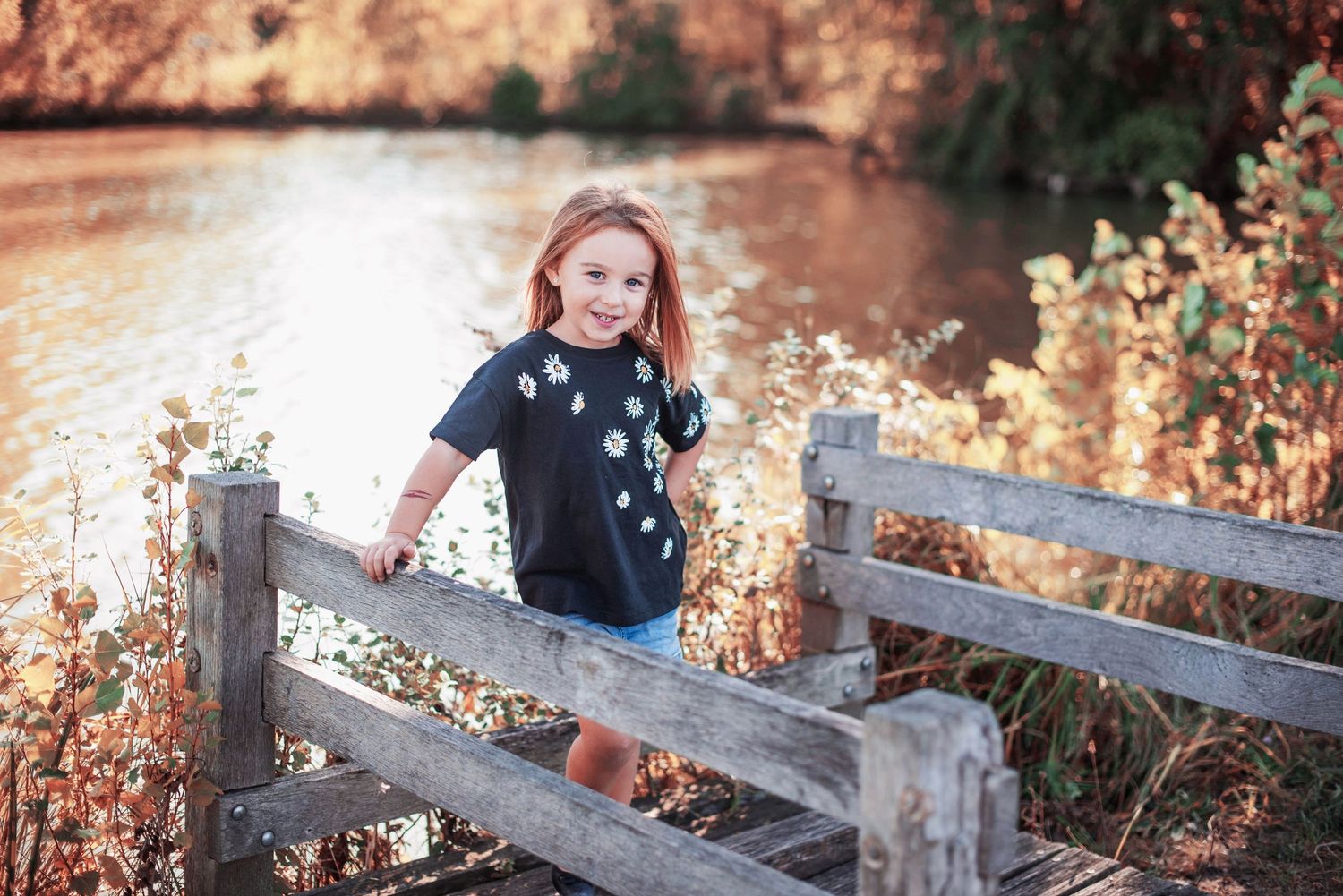 Child sitting on rustic wooden fence during autumn photoshoot.