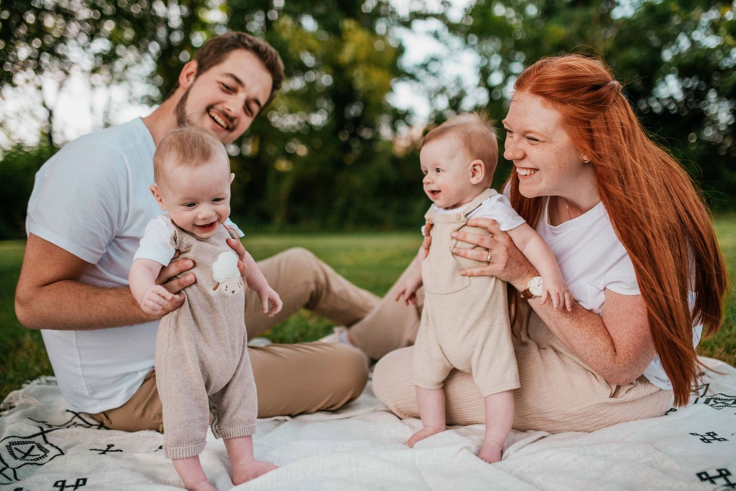 Family lying together on a white blanket outdoors during a lifestyle photography session.