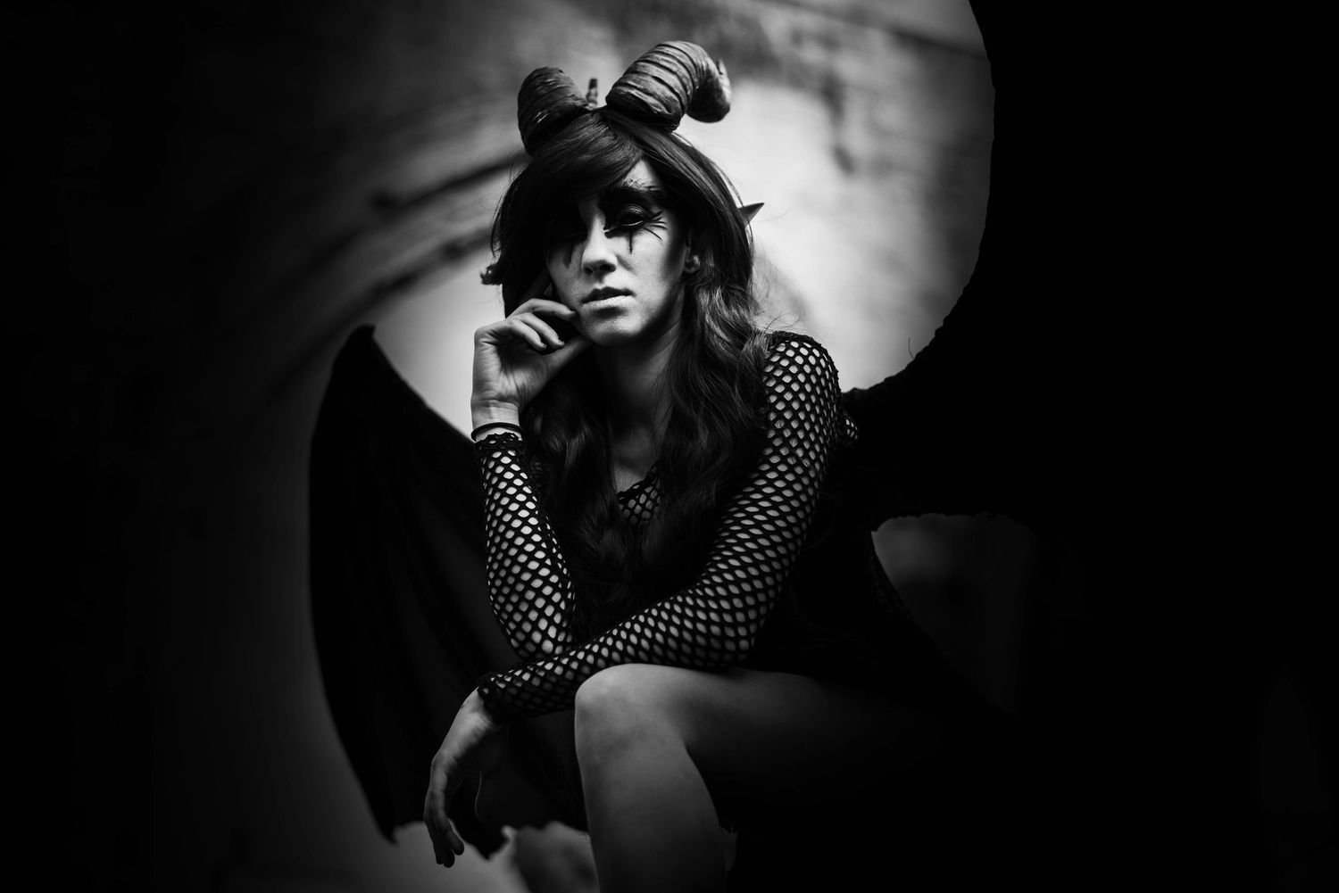 Moody black and white portraits of gothic figure with bat wings in dramatic lighting.