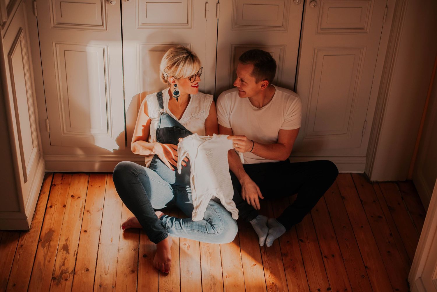 Cozy indoor maternity session photographed on wooden floors with warm lighting.