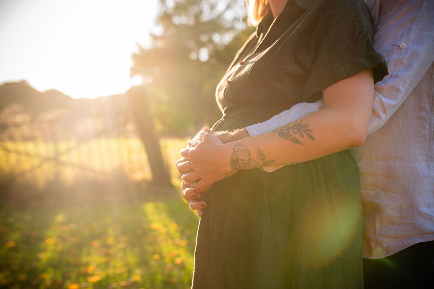 Couple embraces during golden hour sunset photoshoot in a natural outdoor setting.