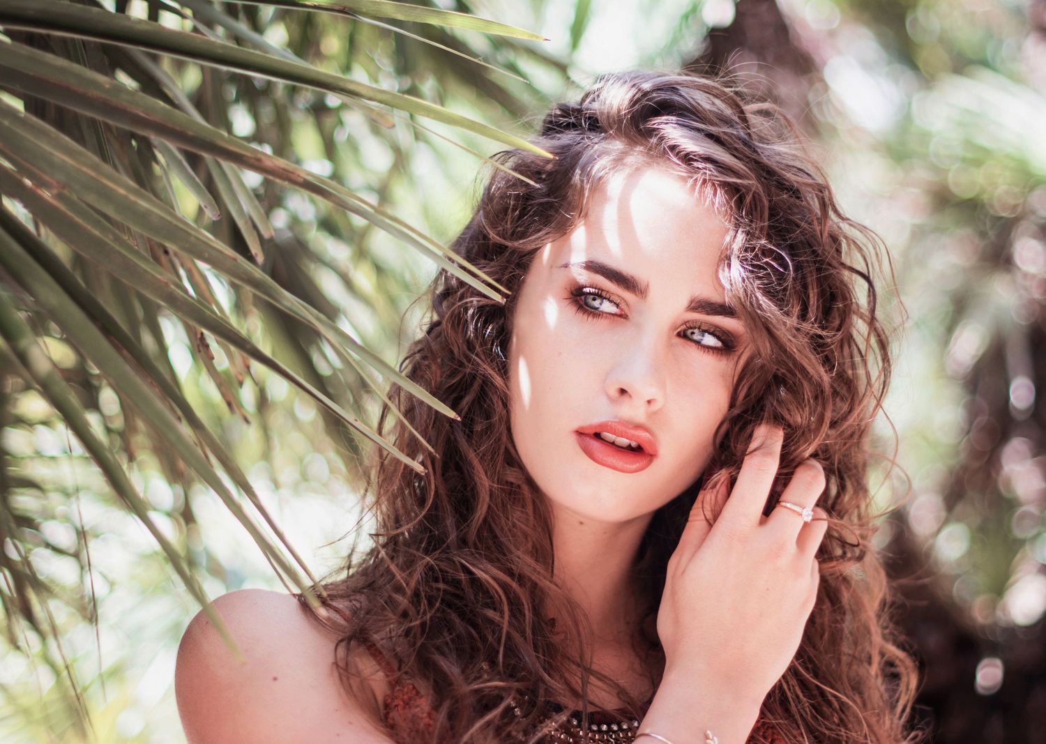 Sun-dappled portrait under palm fronds with natural lighting and bohemian styling.
