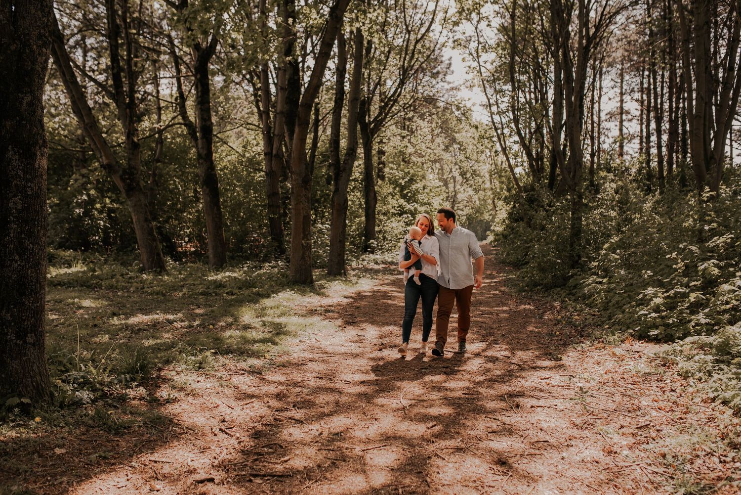 Wooded path with dappled sunlight showing silhouettes walking in distance.