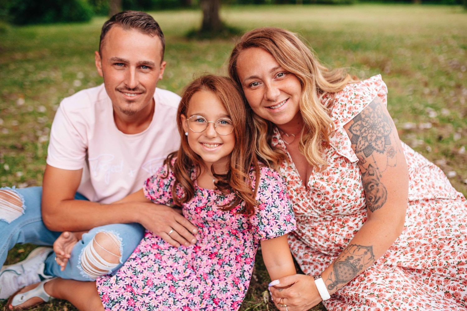 Family wearing coordinated floral outfits poses together in a sunny outdoor setting.