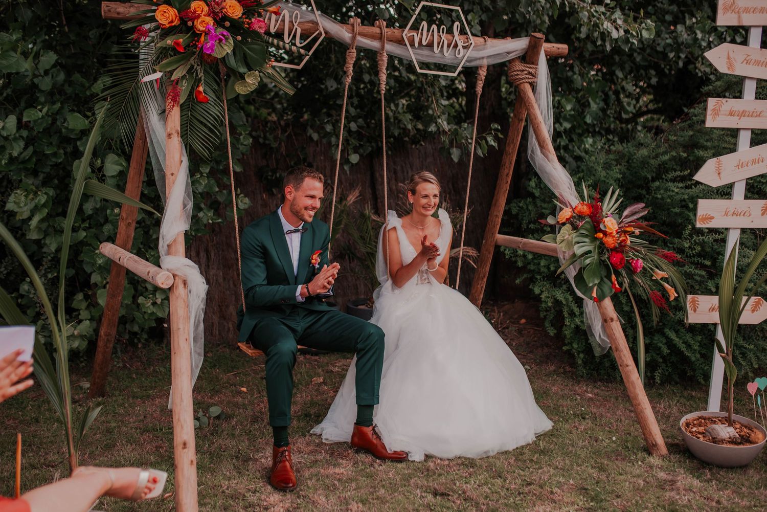 Wedding couple poses playfully with wooden directional signs in a rustic outdoor setting.