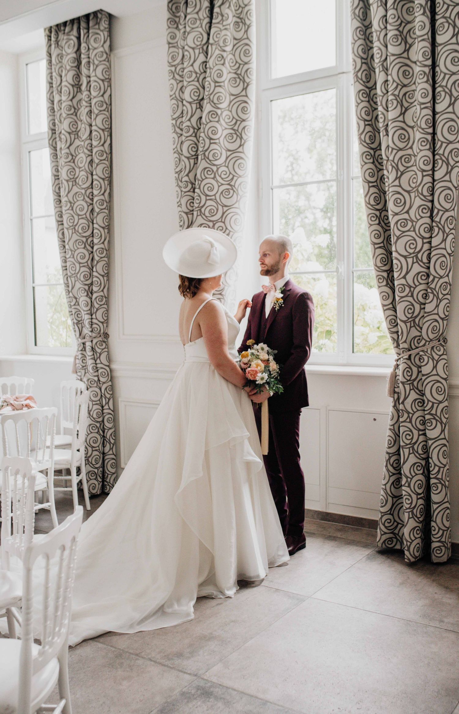An elegant wedding scene with flowing curtains and natural light streaming through tall windows.