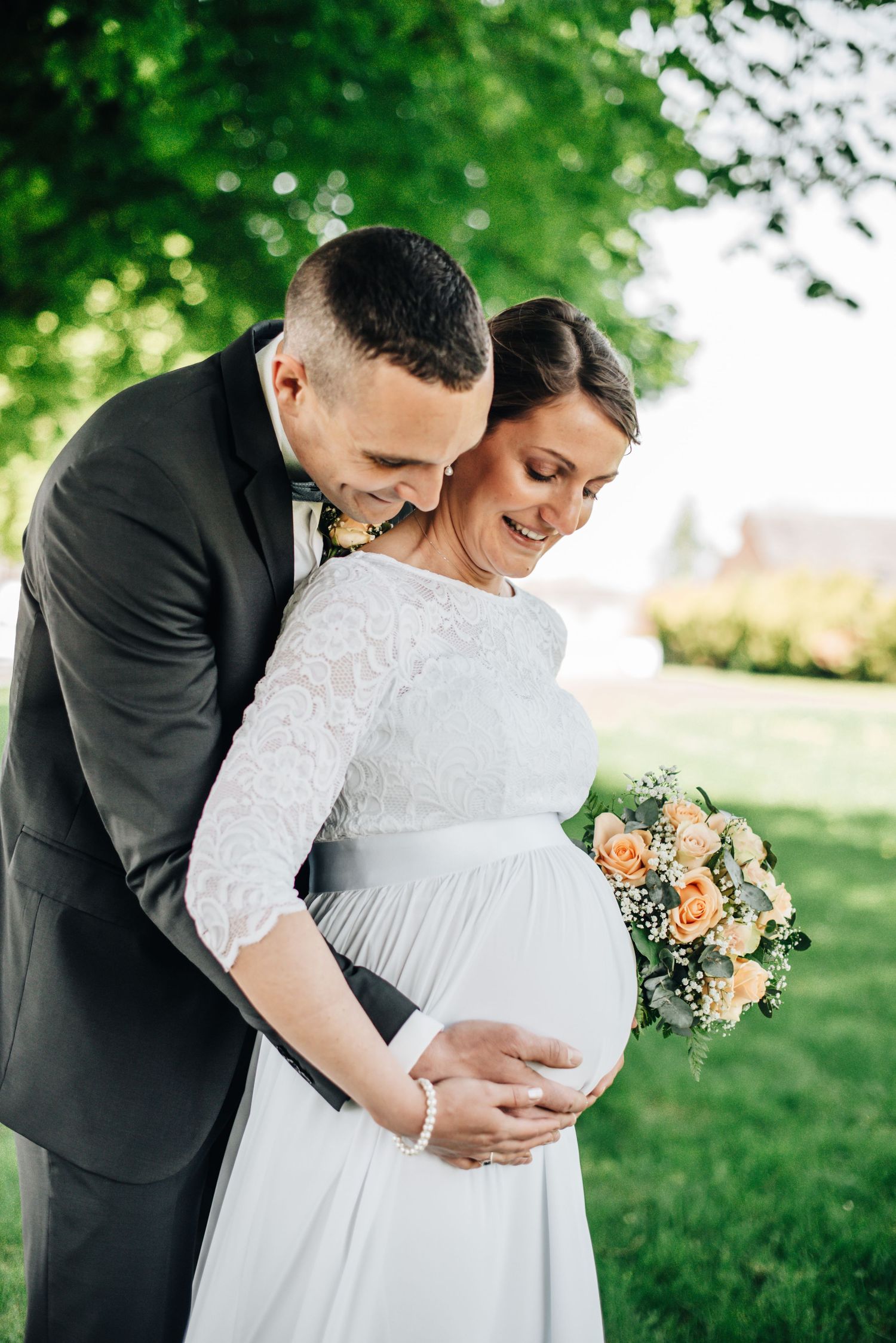 Romantic maternity wedding photos captured under lush green trees.
